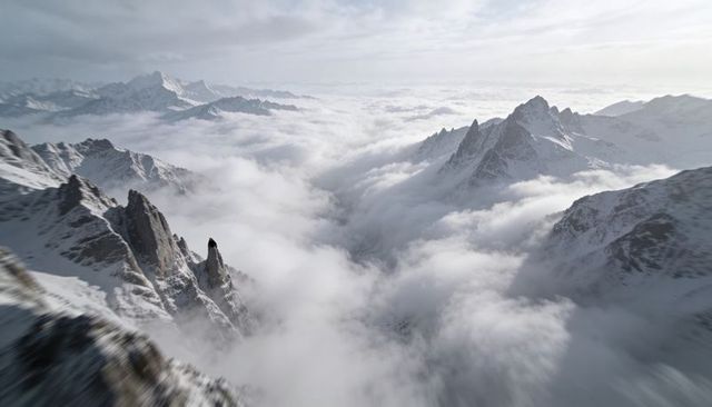 Aerial Jagged Snow-Covered Peaks Rising Above Sea of Clouds Over Remote Alpine Valley
