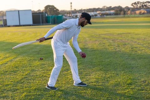 Cricketer picking up ball during golden hour practice on sunlit outfield, training drill