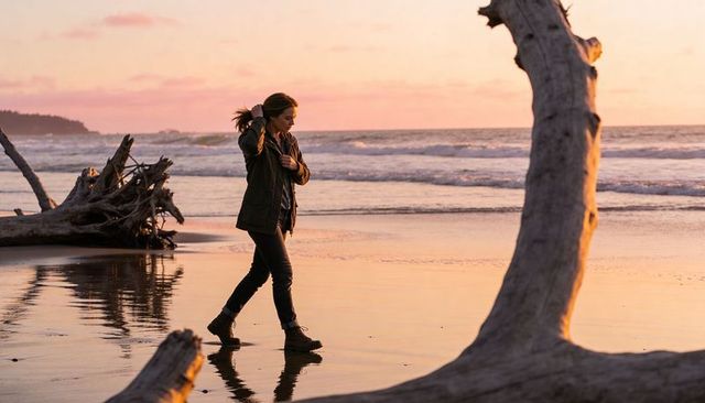 Woman walking along sunset beach with driftwood and reflective wet sand