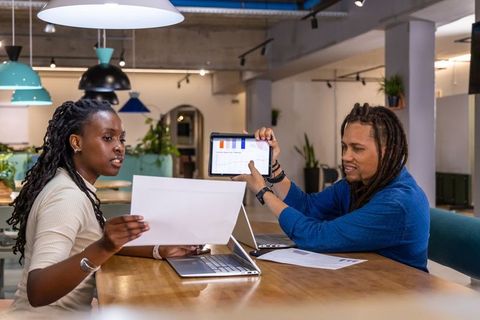 African American coworkers collaborating over laptop and tablet reviewing charts and data