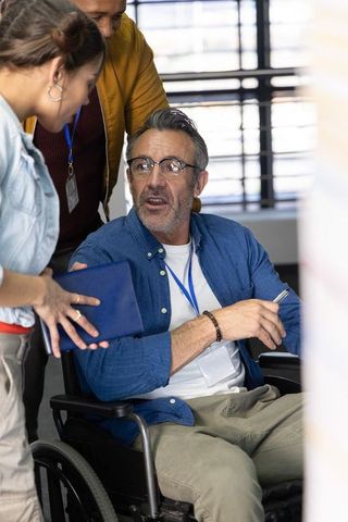 Wheelchair user leading collaborative office meeting with colleagues wearing lanyards