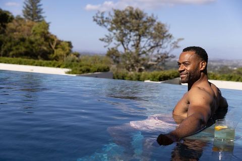 Relaxing african american man reclining in infinity pool at luxury villa with scenic view