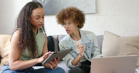African american women collaborating with tablet and laptop on home couch, remote teamwork