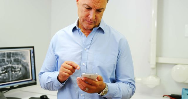 Male Dentist Using Smartphone in Clinic with Dental X-Ray on Monitor - Download Free Stock Images Pikwizard.com