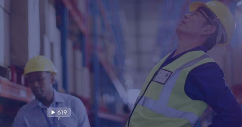 Leaning back inspecting warehouse racks wearing high-visibility vest and hard hat