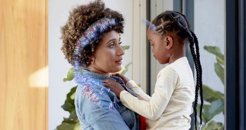 Mother and daughter sharing tender moment by sunlit glass door, gentle embrace at home