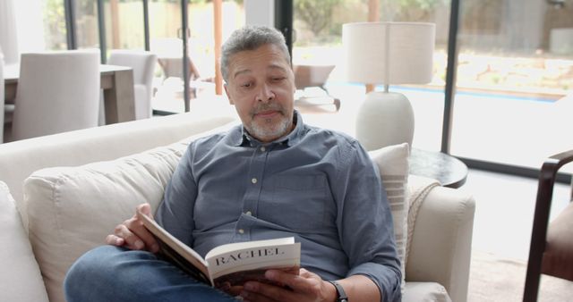 Middle-aged man reading a book on sofa in bright living room - Download Free Stock Images Pikwizard.com