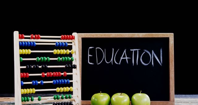 Colourful abacus and blackboard with 'EDUCATION' text in white chalk, accompanied by green apples on wooden table. Useful for educational websites, school materials, back-to-school promotions, early learning features, and teaching resources.
