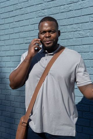 African american man standing and talking on phone wearing gray polo and brown satchel