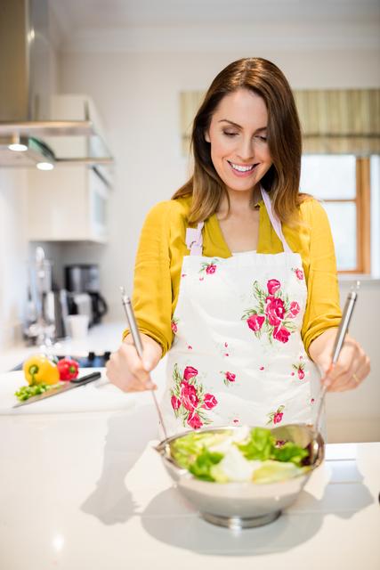 Happy woman preparing salad in kitchen at home