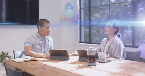 Colleagues collaborating over tablets in bright minimalist office with pastel balloons