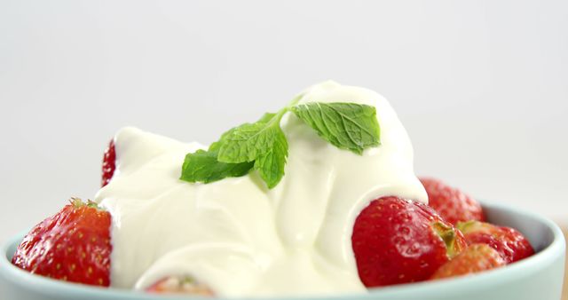 Fresh strawberries are topped with creamy yogurt and garnished with a sprig of mint, with copy space. A healthy and refreshing snack option, this dish combines the sweetness of ripe fruit with the tanginess of yogurt.