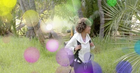 Woman hiking in sunlit tropical forest clearing with backpack and rolled pad, looking right