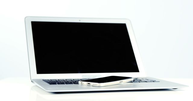 Image showing open laptop with smartphone placed on its keyboard on white background. Useful for concepts like modern technology, digital lifestyle, multitasking, and work-from-home setups. Ideal for use in articles, blogs, or advertisements related to tech devices, productivity, and remote work.
