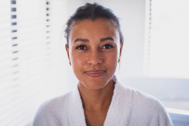 Portrait of biracial woman wearing bathrobe looking to camera and smiling. staying at home in isolation during quarantine lockdown.