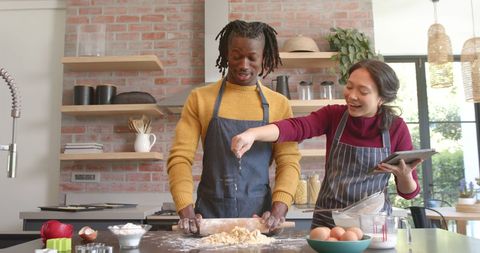 Happy diverse couple baking together using tablet for recipe
