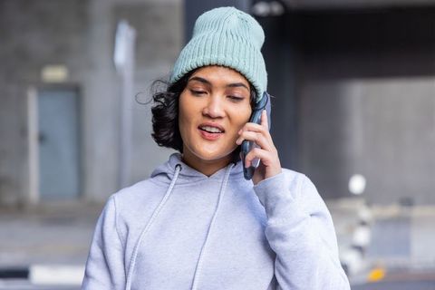 Young woman in mint beanie talking on smartphone at urban underpass wearing gray hoodie