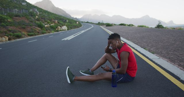 African american man holding smartphone taking a break from running on the road. fitness sports and healthy lifestyle concept