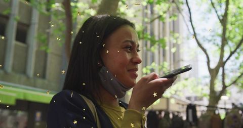 Urban woman speaking into smartphone with mask under chin, sunlit street market moment