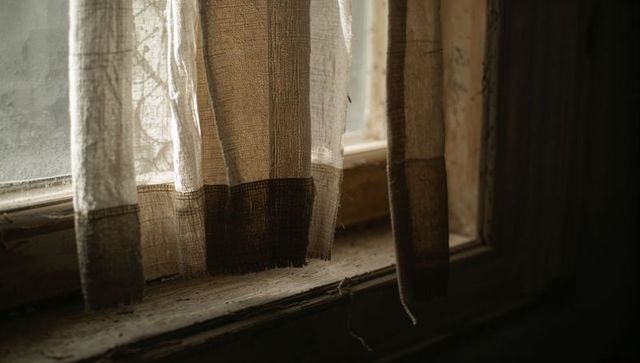 Sunlit Sheer Linen Curtain with Brown Hem Casting Soft Light over Weathered Window Sill
