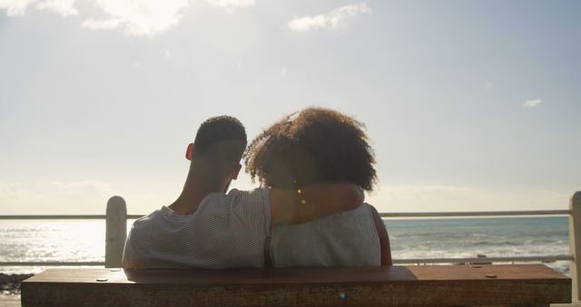 Romantic diverse couple sitting,embracing and looking on sea on sunny promenade, copy space. Summer, vacation, romance, love, relationship, free time and lifestyle, unaltered.