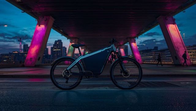 Matte dark e-bike with built-in battery beneath neon-lit bridge at twilight