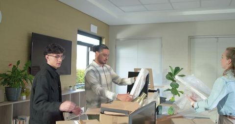 Diverse team unpacking office equipment and installing monitors in bright workspace