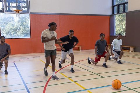 African american basketball team training with coach doing lunges on indoor gym court