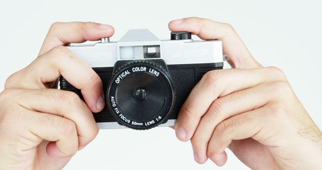 A close-up of hands holding a vintage film camera, focusing on the optical color lens. Ideal for photography workshops, hobby magazines, photography blog posts, or articles on retro photography techniques and equipment. Suitable for promoting photography courses or vintage camera collections.