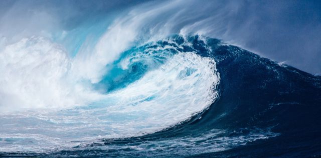 This image captures the majestic beauty of a large ocean wave crashing with incredible force against a backdrop of a clear blue sky. The composition highlights both the power and graceful movement of the ocean, making it ideal for use in nature-related content, marine conservation campaigns, surfing publications, travel brochures, or inspirational visuals that emphasize the beauty and strength of natural elements.