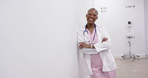 Smiling doctor leaning in bright hospital corridor wearing pink scrubs and stethoscope