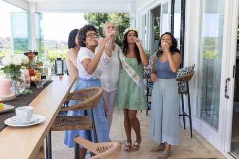 Bridal shower friends toasting with champagne on sunny balcony celebrating bride-to-be
