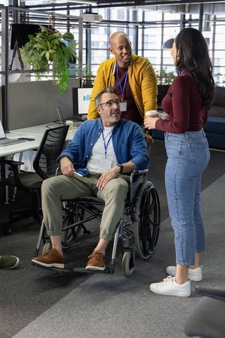 Diverse team collaborating with colleague in wheelchair in modern accessible office