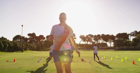 Female Soccer Player Training at Sunset on Field with Cones