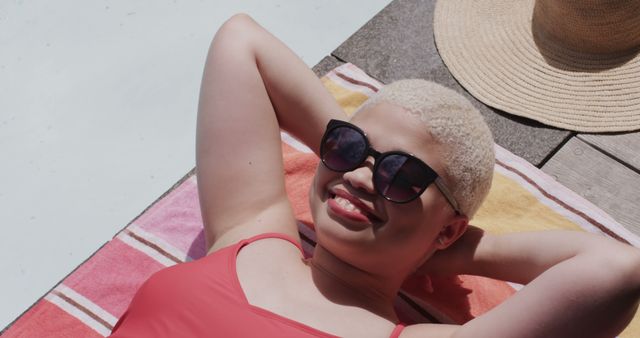 Happy biracial woman with sunglasses sunbathing lying on towel. Lifestyle, free time, summer and vacation, unaltered.