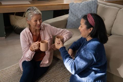 Mature friends sharing coffee and conversation with matching mugs in cozy living room