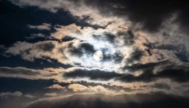 Full Moon Halo Casting Moonbeams Through Layered Clouds Over Dark Night Sky