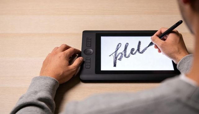 Designer sketching modern lettering on black graphics tablet with stylus at wooden desk