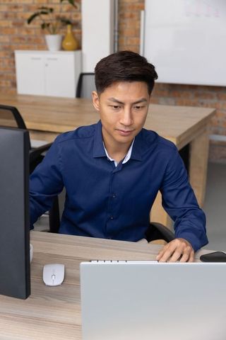 Asian professional working on dual screens in modern office