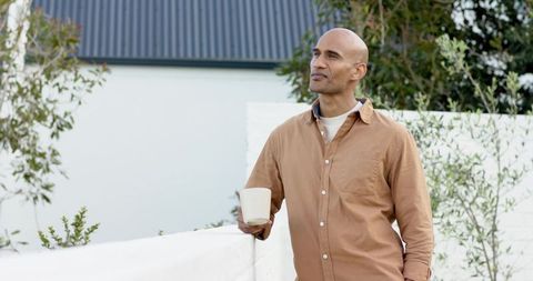 Mature man leaning on white wall holding ceramic mug in tranquil courtyard morning