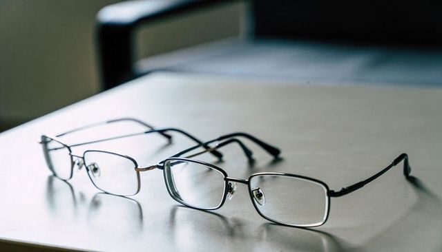 Metal eyeglasses resting on clean tabletop casting soft reflections with blurred pair
