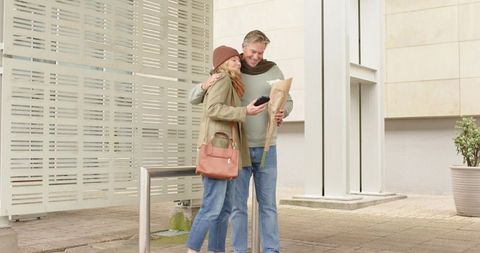 Mature couple embracing while checking phone with bouquet in urban plaza