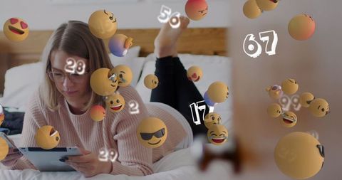 Emojis overwhelming young woman using device on bed