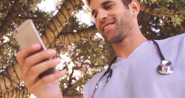 Male doctor using mobile phone in the backyard of hospital