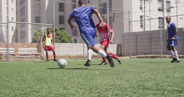 Amateur soccer players engaging in a lively match on a sunny day. The team in red and white stripes is competing against the team in blue uniforms. Suitable for illustrating sports activities, team spirit, outdoor events, and athletic training.
