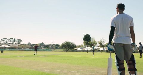 Amateur batsman batting on sunny community cricket field with teammates in background