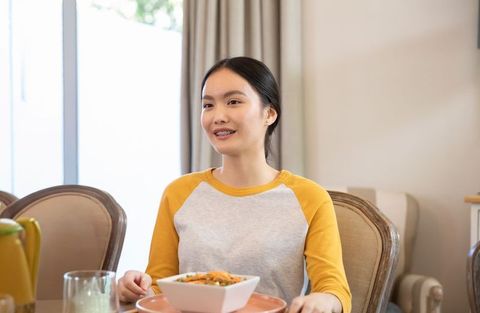 Asian woman smiling with braces at dining table enjoying healthy homemade meal