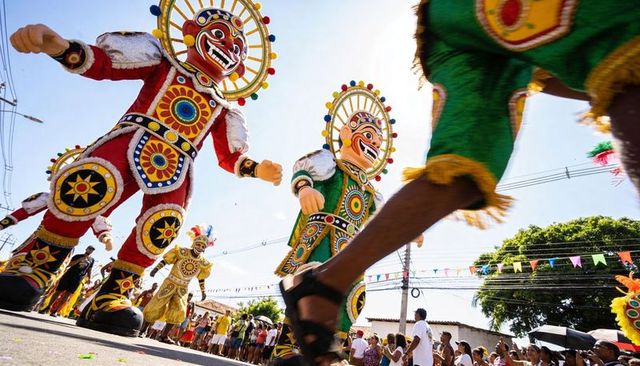 Giant colorful masked figures parading through sunny street during lively carnival
