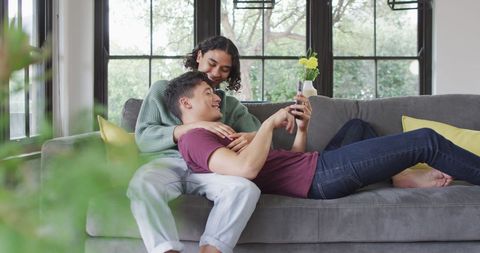 Happy Couple Relaxing on Couch at Home Using Smartphone