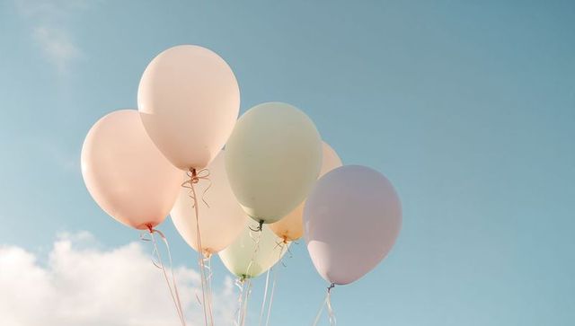 Pastel balloons floating against soft blue sky for minimalist celebration and decor